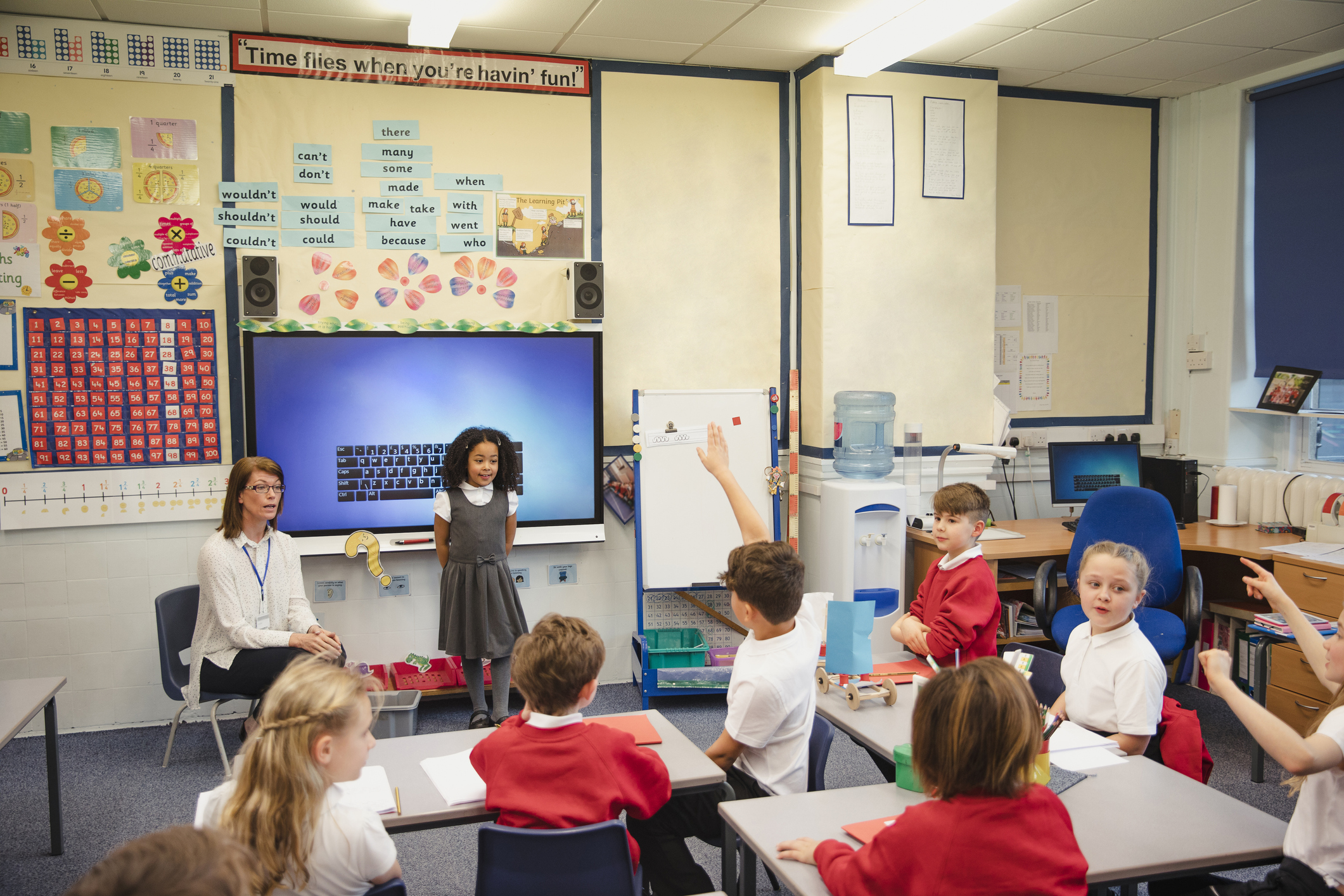 An elementary schoolgirl presents her work to the class with the support of her teacher beside her. This is a school in Hexham, Northumberland in north eastern England.